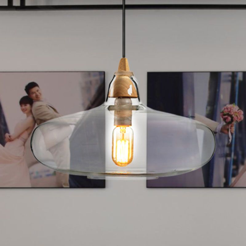 Clérachic saucer pendant in clear glass on its turned wood collar, filament lit above a wall of framed photos.