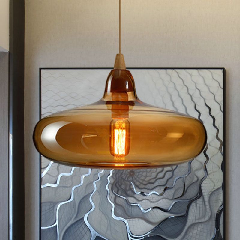 Amber glass saucer pendant by Clérachic, the wide shade catching light in front of a framed line artwork.