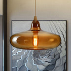 Amber glass saucer pendant by Clérachic, the wide shade catching light in front of a framed line artwork.