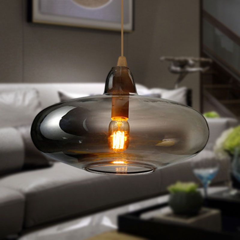 Clérachic saucer pendant in smoke gray glass, glowing over a pale sofa and coffee table in a living room.