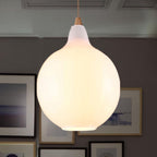Clérachic globe pendant in white opal glass, a full round shade lit softly above a gallery wall of frames.