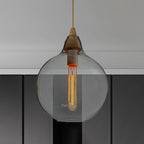 Clear glass globe pendant from Clérachic, tube filament suspended inside, hung over dark kitchen cabinetry.