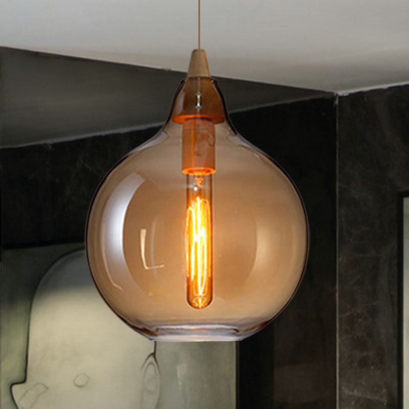 Clérachic globe pendant in amber glass, warm filament centred in the round shade, against a dark stone wall.