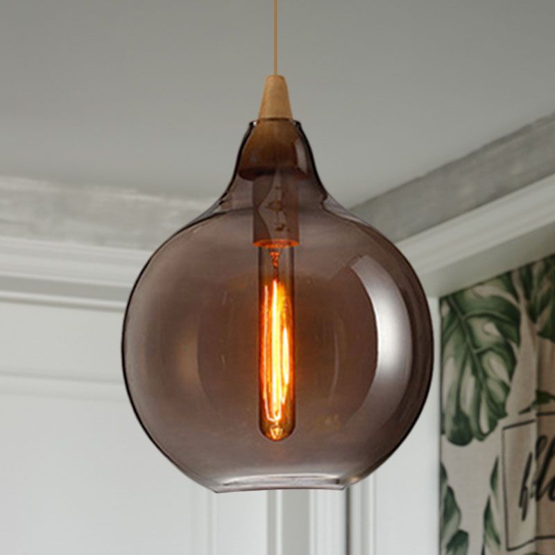 Clérachic globe pendant in smoke gray glass, lit below a white moulded ceiling beside a leaf-print curtain.