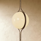 Clérachic floor-to-ceiling lamp in vintage brass, seen at an angle so the ring crosses the lit globe and the second half shows beyond it.