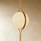 Clérachic floor-to-ceiling lamp in brass, a three-quarter view of the opal globe with the polished ring closing over its join.