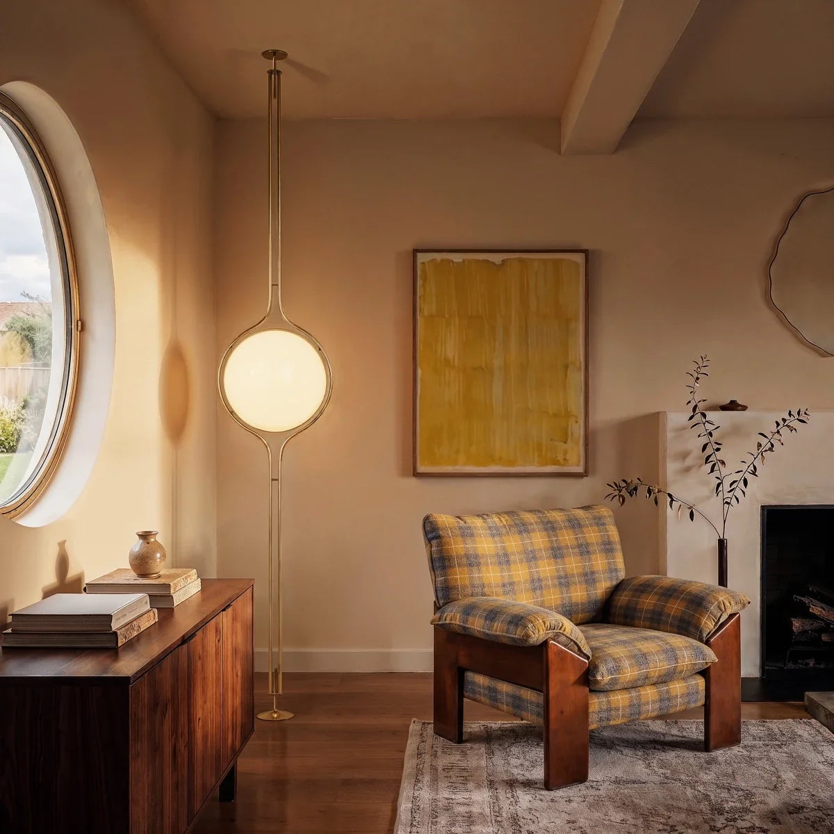 Clérachic floor-to-ceiling lamp in brass, standing between a round window and a plaid armchair, its pole rising to a small round ceiling canopy.