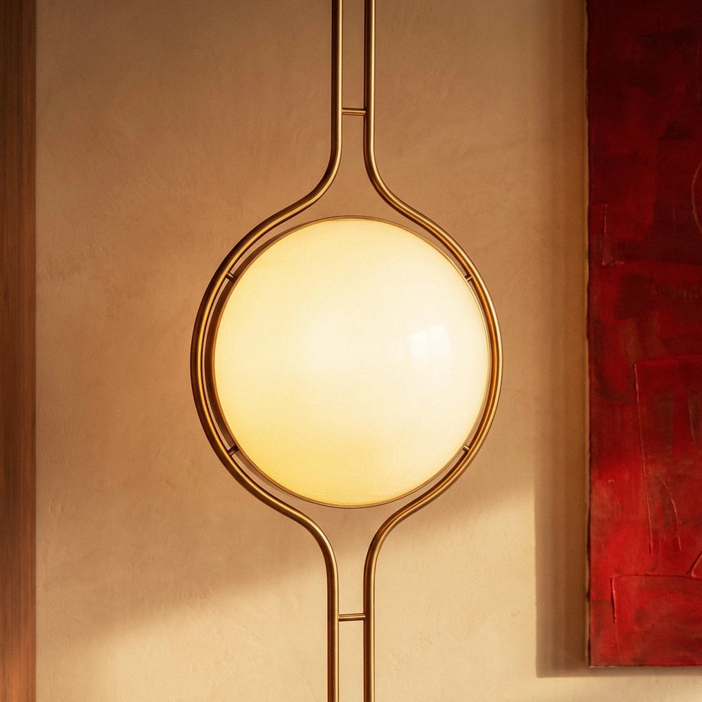 Clérachic floor-to-ceiling lamp in brass, the lit globe framed against the edge of a red painting on a warm plaster wall.