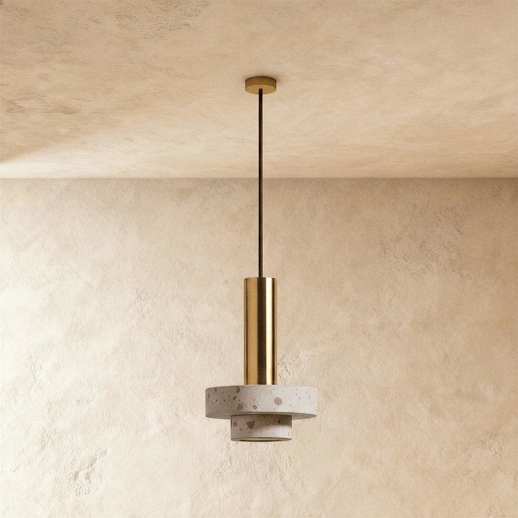 Clérachic gold-toned-and-terrazzo pendant with two stepped speckled stone rings below a slim gold-toned tube, against limewash plaster.