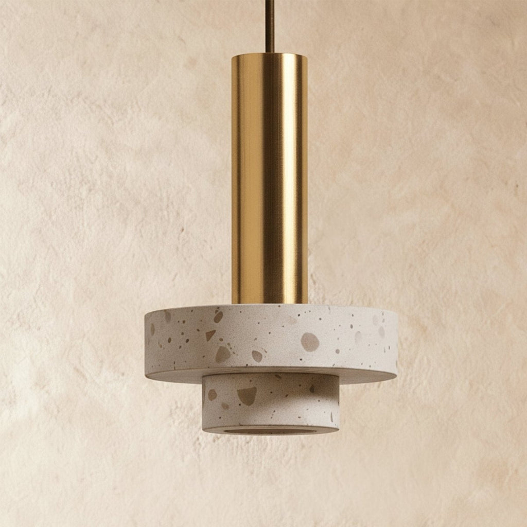 Close view of a Clérachic pendant showing a gold-toned cylinder over stepped, pale speckled terrazzo discs on plaster.