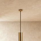 Clérachic gold-toned ceiling rose and slim dark rod leading down to the top of a gold-toned cylinder, against a plaster wall.
