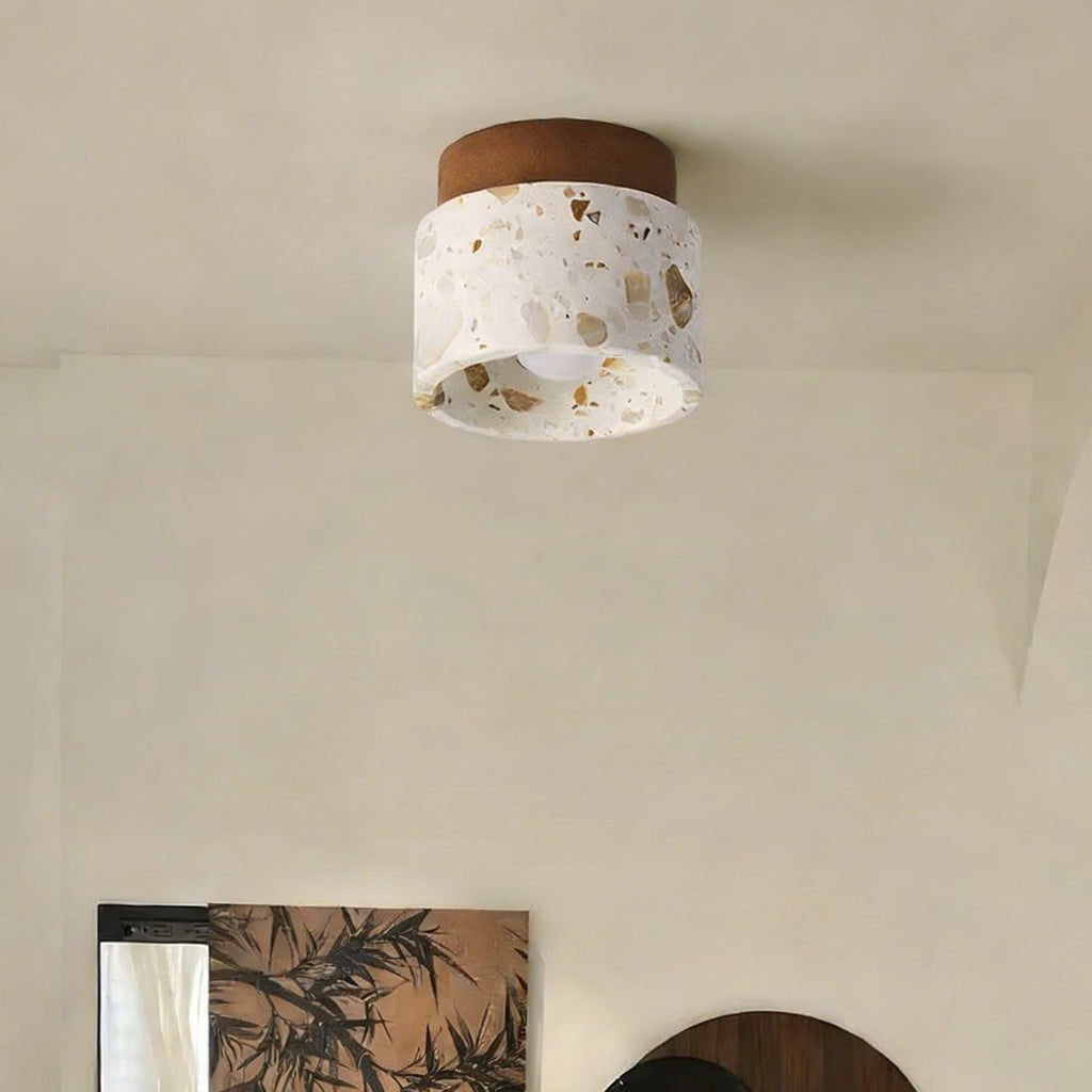 Unlit Clérachic terrazzo ceiling light with a walnut canopy, set in a calm cream room with a leafy print on the wall below.