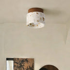 Unlit Clérachic terrazzo ceiling light with a walnut canopy, set in a calm cream room with a leafy print on the wall below.
