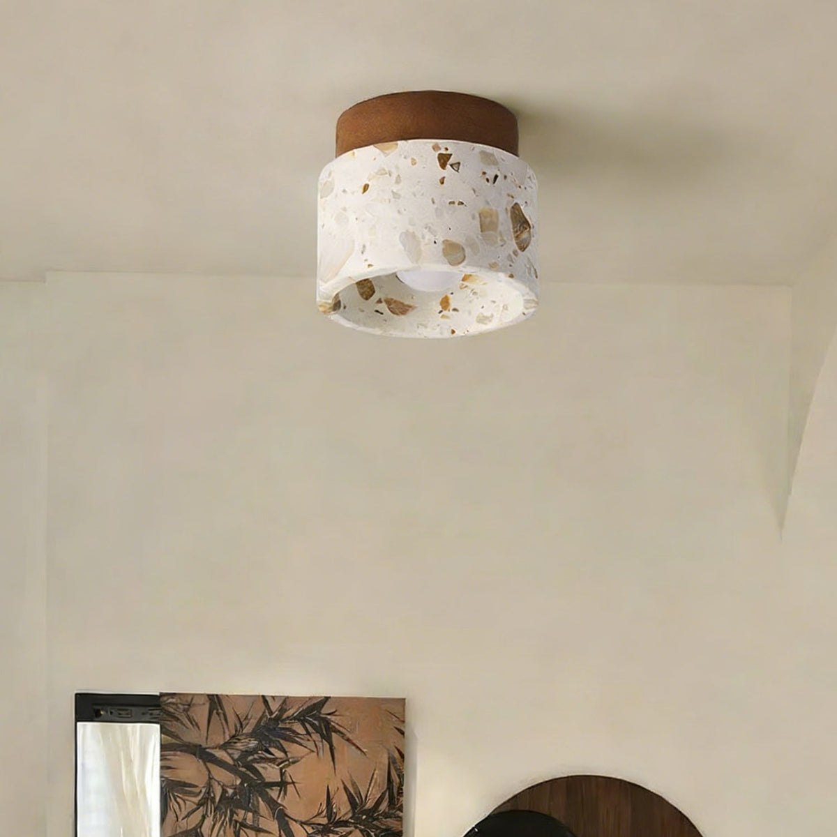 Unlit Clérachic terrazzo ceiling light with a walnut canopy, set in a calm cream room with a leafy print on the wall below.