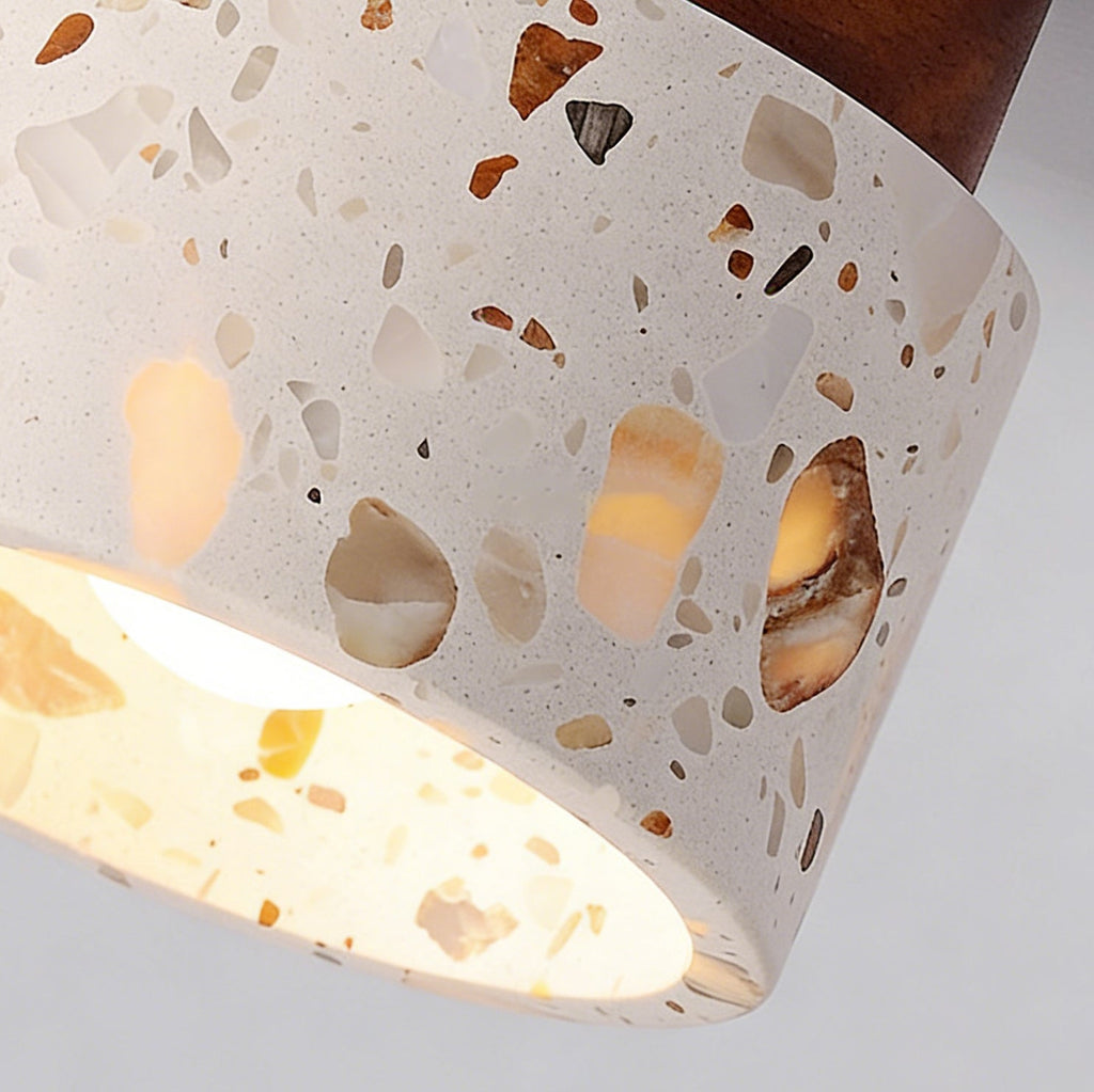 Close view of the chipped stone and amber terrazzo pattern on the shade of this Clérachic ceiling light, with the bulb glowing inside.