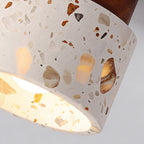 Close view of the chipped stone and amber terrazzo pattern on the shade of this Clérachic ceiling light, with the bulb glowing inside.