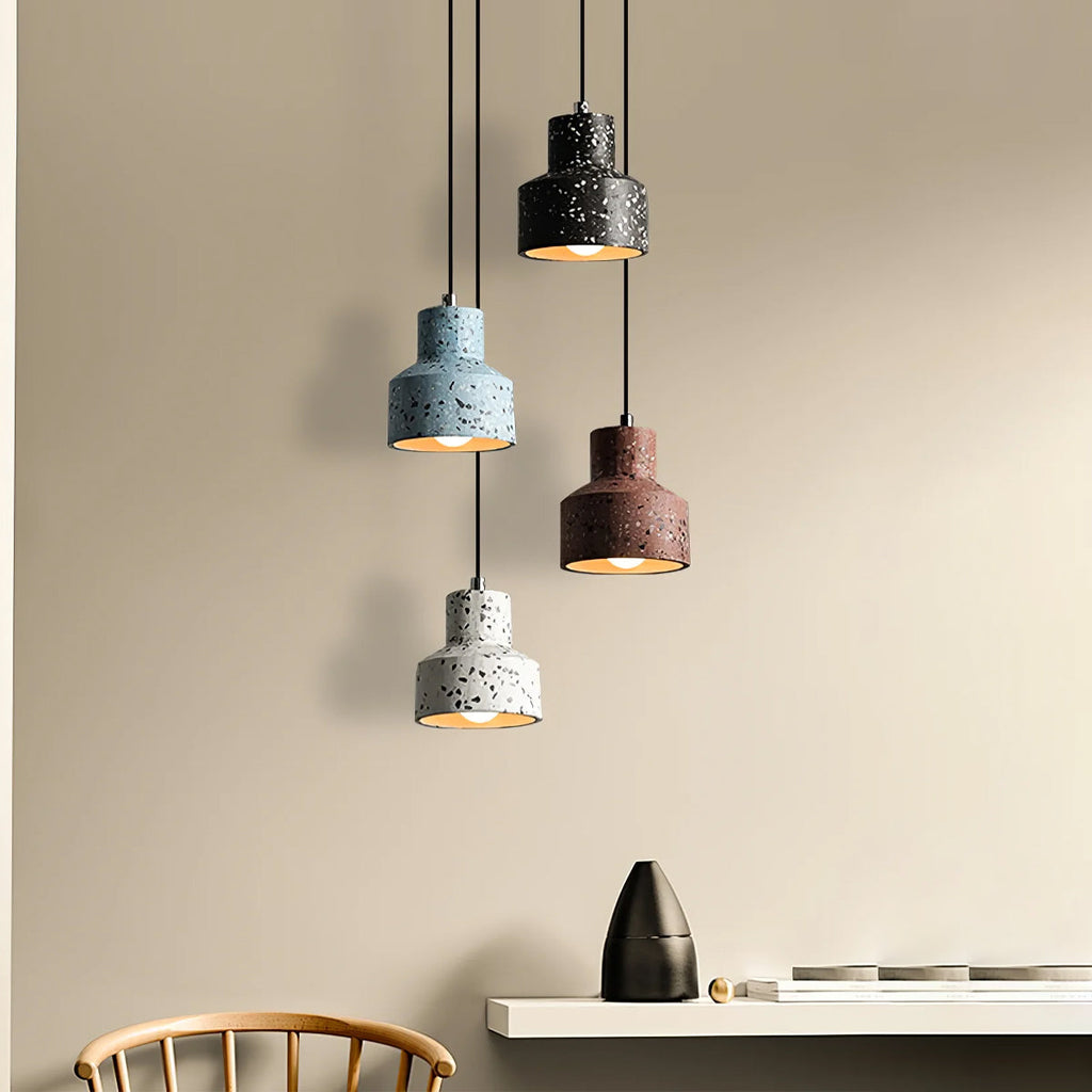 Above a pale shelf and a wooden chair, this Clérachic cluster of speckled pendants hangs in blue, black, red and white against a sand wall.