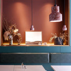 Speckled cement pendants hang in a terracotta alcove with dried flowers and a framed print, one Clérachic shade glowing in the foreground.