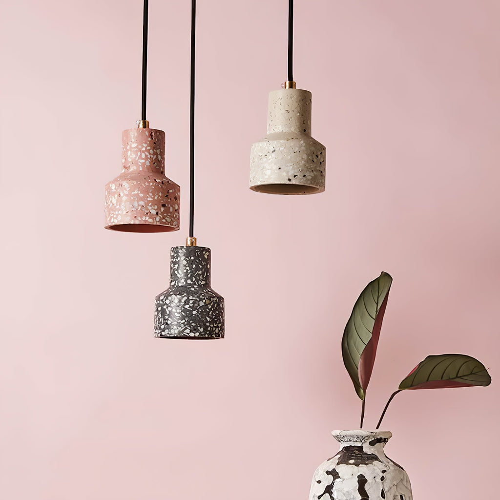 Against a soft pink wall beside a leafy plant, three Clérachic terrazzo pendants hang on black cords in pink, cream and charcoal.