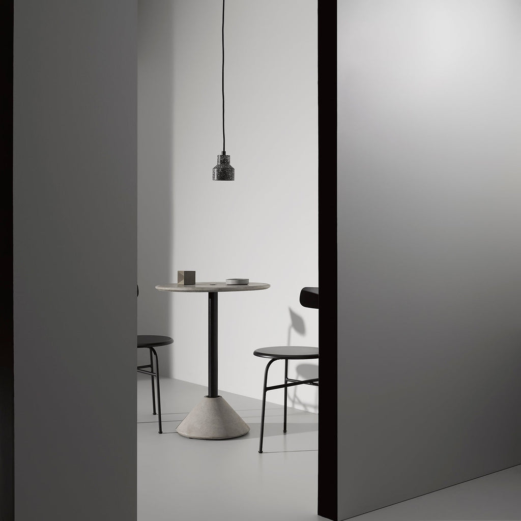 A single dark terrazzo pendant from Clérachic hangs in a grey doorway above a round café table and two black chairs.