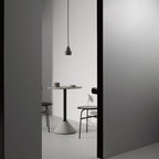 A single dark terrazzo pendant from Clérachic hangs in a grey doorway above a round café table and two black chairs.