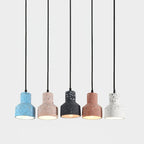 A lit row of five Clérachic pendants on long black cords, each cement shade a different speckled colour with a warm glow inside.