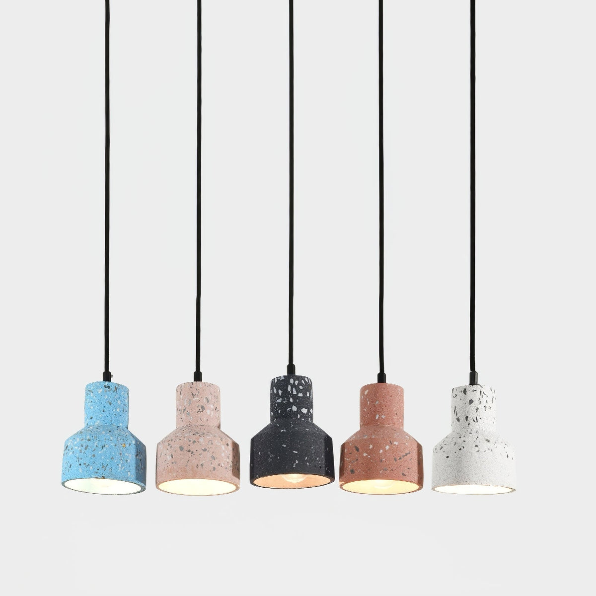 A lit row of five Clérachic pendants on long black cords, each cement shade a different speckled colour with a warm glow inside.
