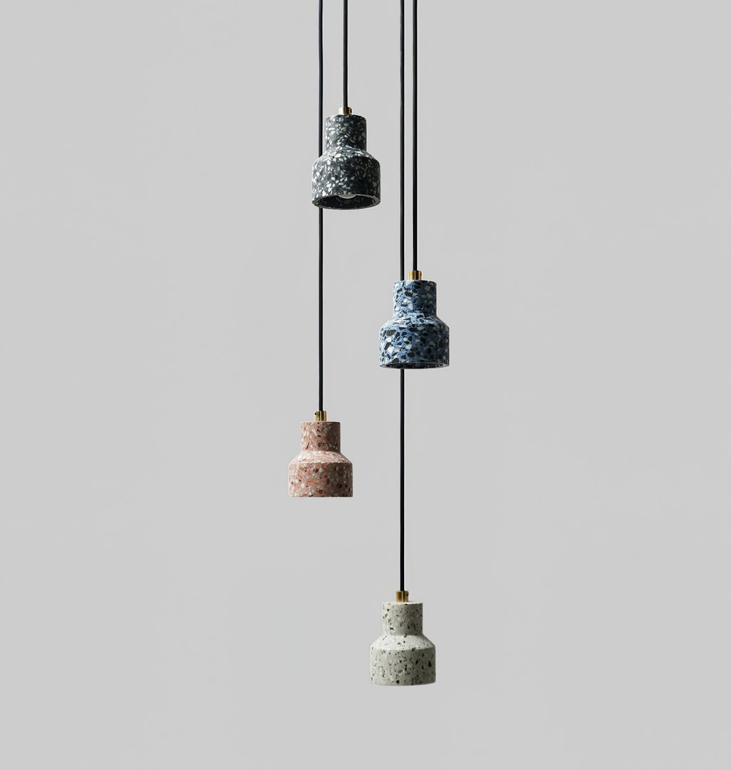 On a grey backdrop, four small Clérachic terrazzo pendants hang at different heights, in dark blue, blue, rose and pale grey.