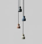 On a grey backdrop, four small Clérachic terrazzo pendants hang at different heights, in dark blue, blue, rose and pale grey.
