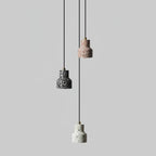 Three Clérachic terrazzo shades in charcoal, rose and white hang at different heights on thin black cords against light grey.