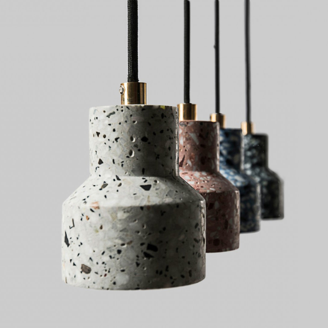Close view of a white terrazzo shade on this Clérachic pendant, with its brass cord fitting and darker shades blurred behind.