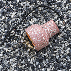 A rose-red terrazzo shade from Clérachic lies on its side on dark gravel, its black cord trailing and the warm inner lining showing.