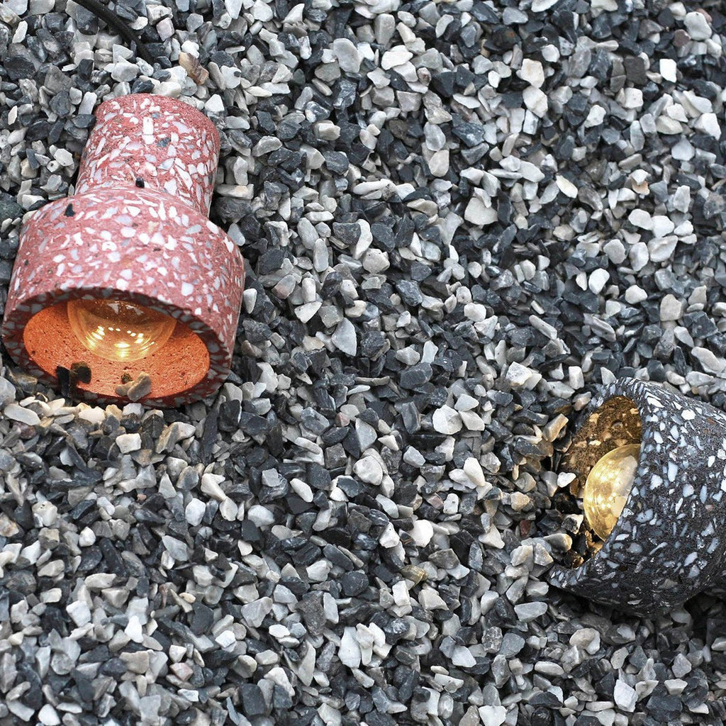 Two terrazzo shades from Clérachic on gravel, one rose-red with a bulb visible inside and one dark with a brass lampholder.