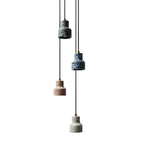 Four Clérachic terrazzo pendants on a white backdrop, hanging on black cords at staggered heights in black, blue, rose and grey.