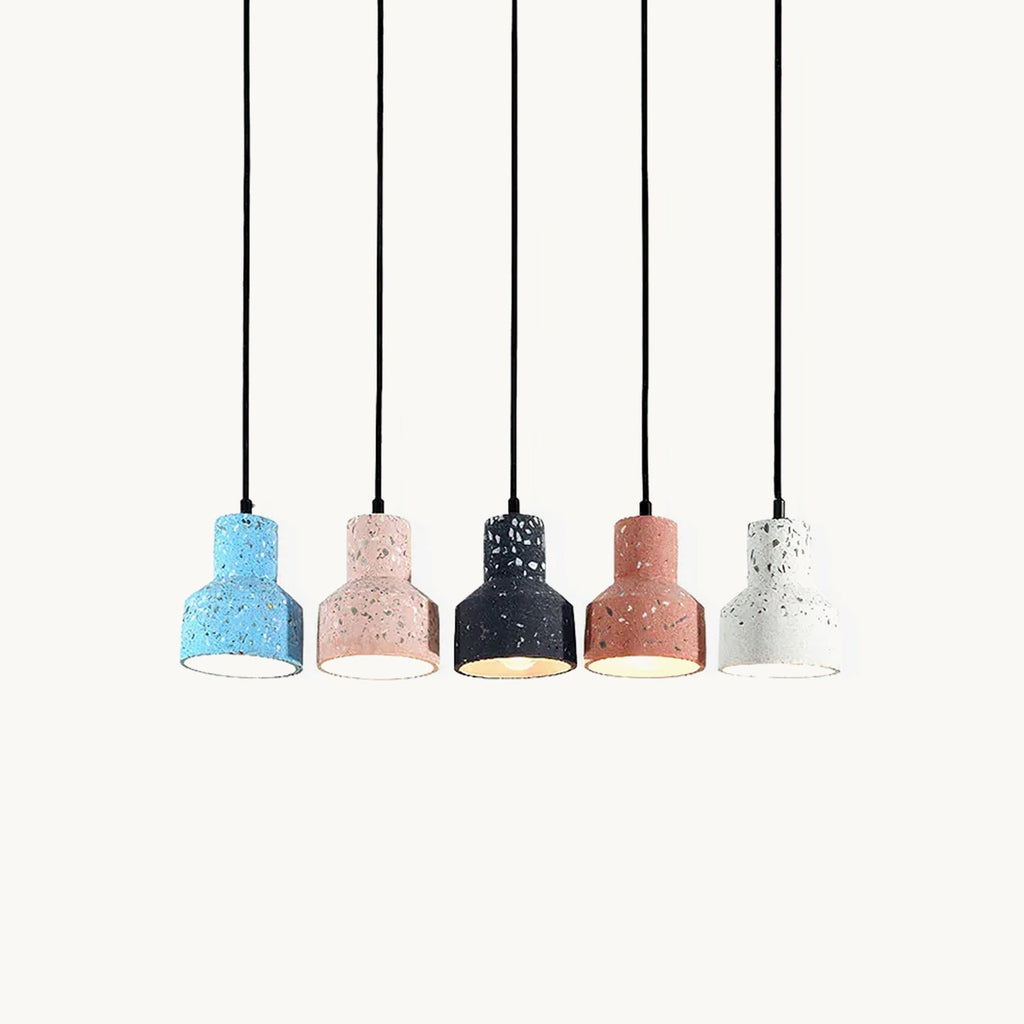 Five Clérachic terrazzo pendants in a row on black cords, in blue, pink, black, salmon and white, with a warm glow from the black one.