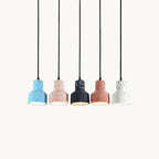 Five Clérachic terrazzo pendants in a row on black cords, in blue, pink, black, salmon and white, with a warm glow from the black one.
