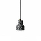 A single charcoal terrazzo pendant from Clérachic hangs on a black cord with a brass fitting, its shade flecked with white chips.
