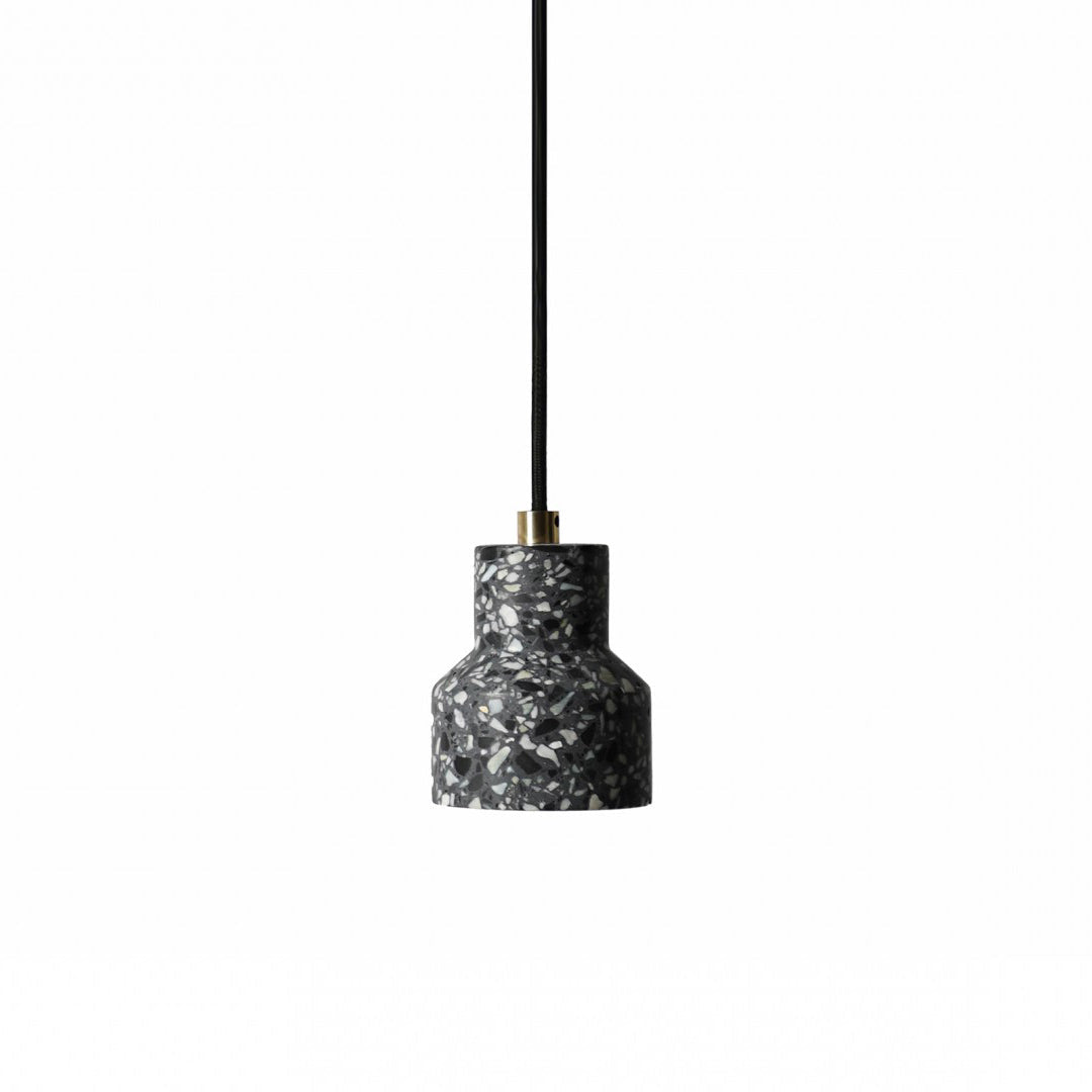 A single charcoal terrazzo pendant from Clérachic hangs on a black cord with a brass fitting, its shade flecked with white chips.