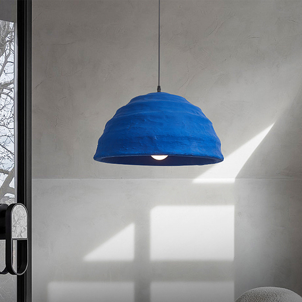 Clérachic Textured Blue Dome Pendant Light glowing against a sun-striped plaster wall beside a glazed door in a quiet living room.
