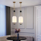 Two Clérachic white pendants hanging side by side in a grey panelled dining room, above a black marble table and a banquette.