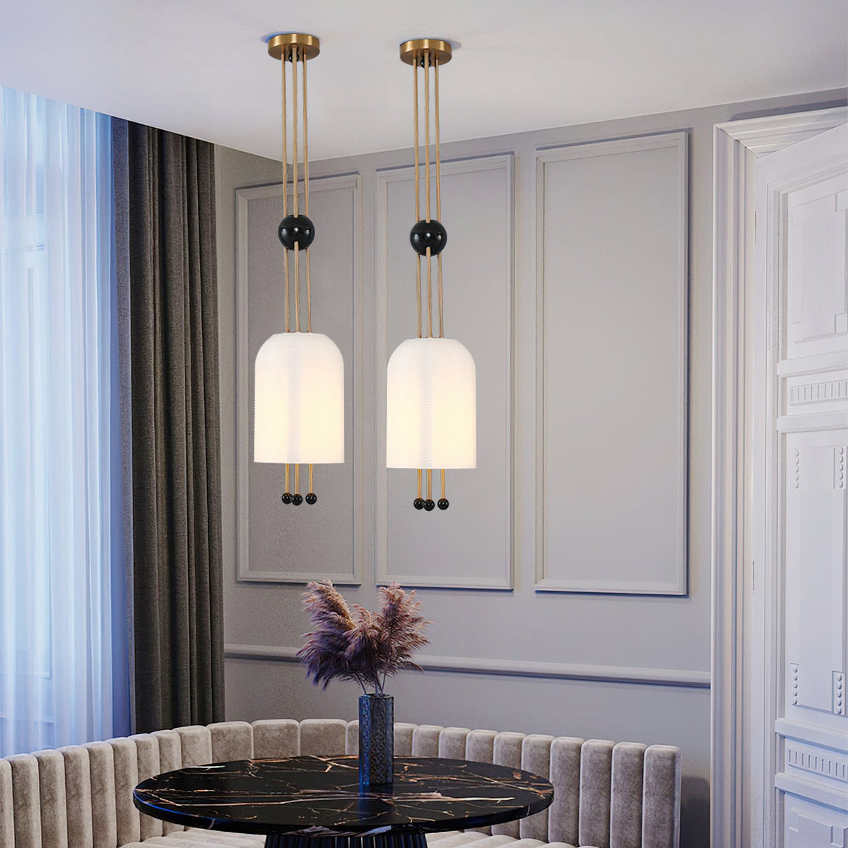 Two Clérachic white pendants hanging side by side in a grey panelled dining room, above a black marble table and a banquette.