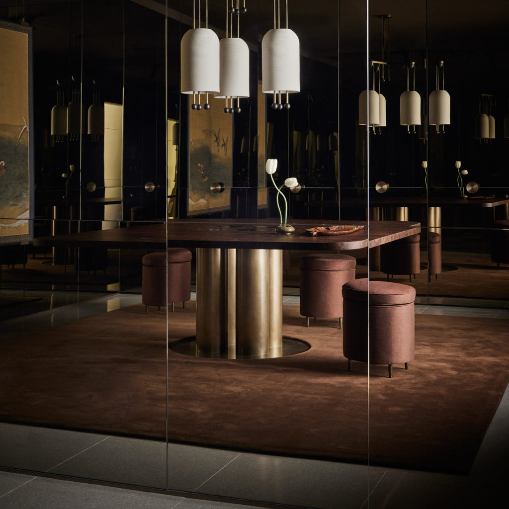 Several Clérachic white pendants hanging in a dark, mirrored room above a round table with brown velvet stools on a deep rug.