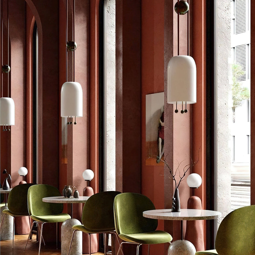 Two Clérachic pendants at different heights in a terracotta-walled café, with olive-green chairs and small round marble tables below.