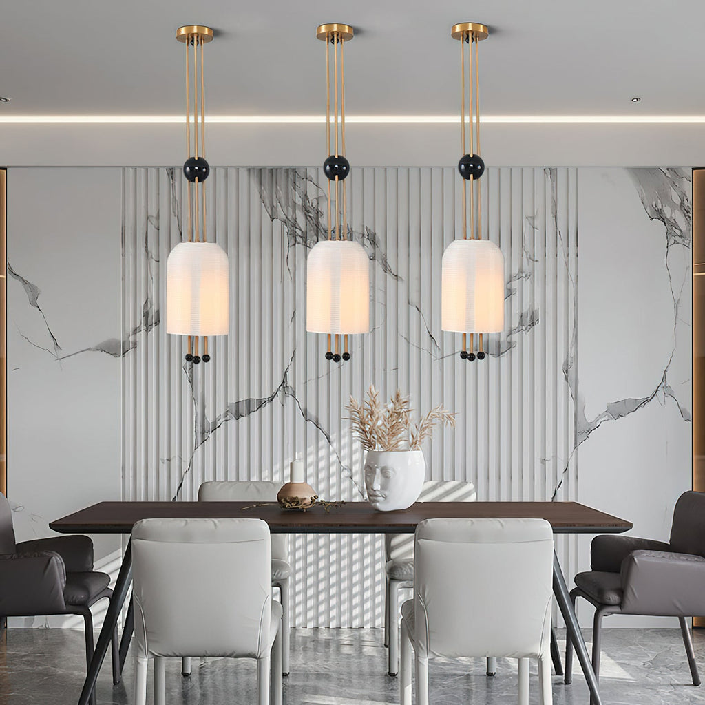 Three Clérachic pendants in a row against a marble-patterned fluted wall, above a dark dining table with pale grey chairs.