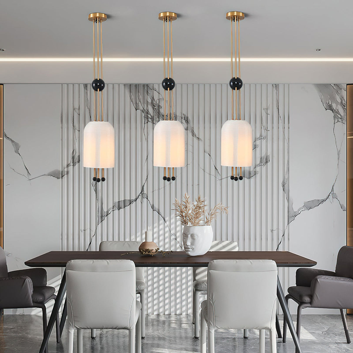 Three Clérachic pendants in a row against a marble-patterned fluted wall, above a dark dining table with pale grey chairs.