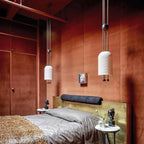Two Clérachic pendants hung at different heights in a rust-red room, with a bed in grey linen and a leopard-print throw below.