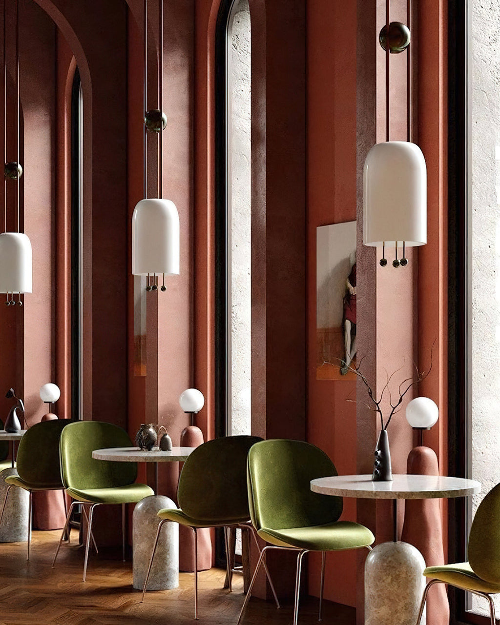 A tall terracotta café with two Clérachic white pendants at different heights, over round marble tables and olive-green chairs.