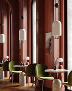 A tall terracotta café with two Clérachic white pendants at different heights, over round marble tables and olive-green chairs.