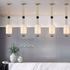 A row of five Clérachic white pendants hung from brass canopies above a pale marble counter, with a grey wall and a vase of foliage.