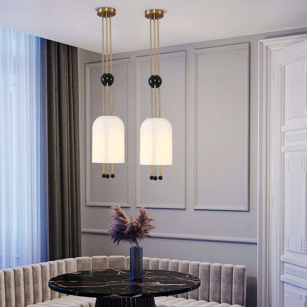 Close-up of two Clérachic white pendants lit in a grey panelled room, with a black marble table and a pale banquette below.